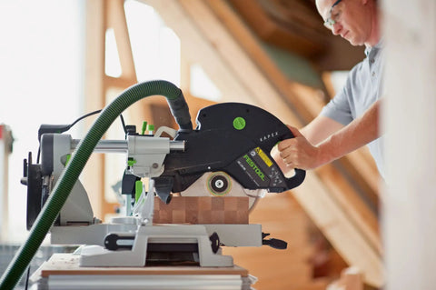 Person using KAPEX KS 120 REB Sliding Compound Miter Saw With Rail Forward Design for precise miter cutting in a workshop