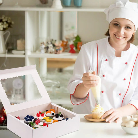 Baker using icing to decorate cupcake near six pack cupcake boxes with windows hold twelve cupcakes bakery grade cardboard containers