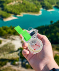 Hand holding Mini Thumb Compass For Outdoor Adventures, Fast Positioning Pocket Navigation Tool, Waterproof Acrylic Trail Boss near a lake.