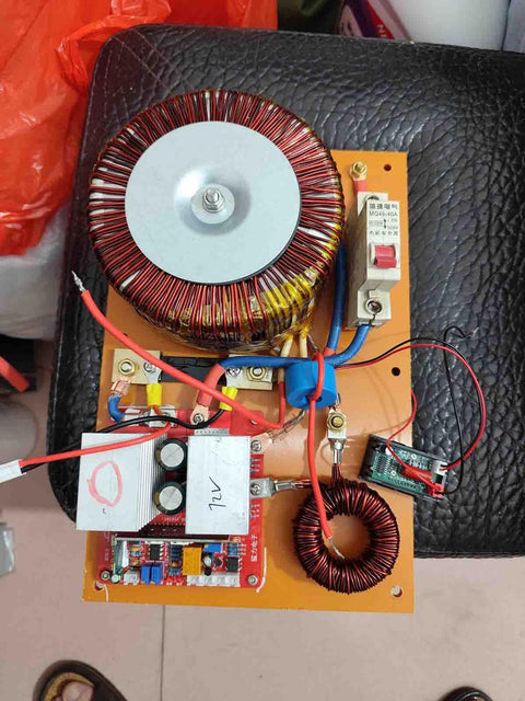 Electronic circuit board with red and yellow coils and blue wires on a black textured surface