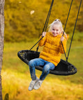 Girl in yellow jacket swinging on 40 Inch Flying Saucer Tree Swing For Kids Heavy Duty Outdoor Disc Round Swing Supports Up To 220 Lbs