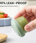 Close-up of hand holding green sauce cup from Eight Pack 2 Oz Salad Dressing Containers To Go With Lids For Lunch Boxes And Bento.