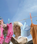 Woman hanging laundry using No Mess Plastic Clothes Pins 48 Pack Heavy Duty Workhorse Colored Laundry Clips on a clothesline outdoors.