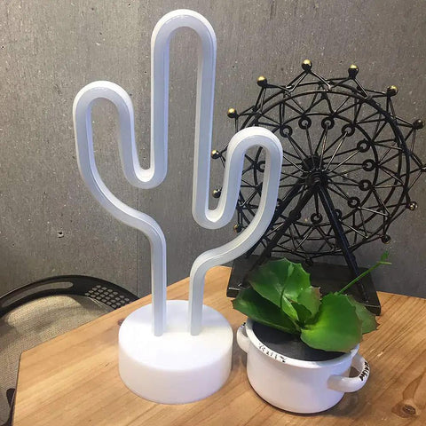 Cactus Neon Night Light With Pedestal LED Sign For Kids Room And Bedroom Decor, Battery Or USB Operated Safe, Cool Low Voltage Neon Light, Green Glow For Parties, Sleepovers, And Weddings. On a table with decorative items.
