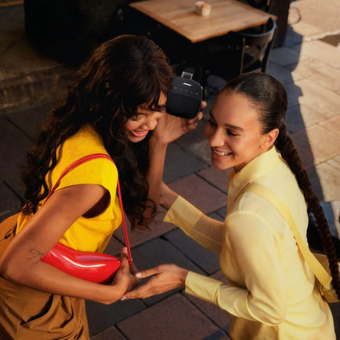 Two women laughing outdoors while holding a SoundLink Micro Portable Bluetooth Speaker 2nd Gen For Outdoors, Black For Adventure