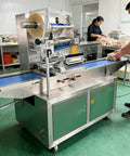 Smooth Operator Compact Horizontal Flow Pack Machine Small Shrink Wrapper in use, sealing packages on counter, busy kitchen setting.