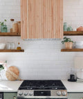Kitchen with wooden range hood and floating shelves with decor items on white tile backsplash