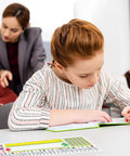 Student writing at desk with Stick On Nameplate Pockets For Desks, 40 Pack, Clear Adhesive Covers Measuring 4.7 X 14.2 Inches