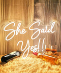 She Said Yes Neon Sign Large 23x16 Inch Warm White LED Flex Neon Light on a cozy fur setting with bottles and glasses.