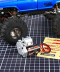 180 Motor 32T Transmission Metal Gearbox Combo For FCX24 Smasher V2 Monster Truck next to a blue monster truck on grid surface