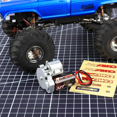 180 Motor 32T Transmission Metal Gearbox Combo For FCX24 Smasher V2 Monster Truck next to a blue monster truck on grid surface