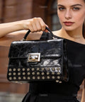 Model holding a black leather handbag adorned with stylish rivet studs, showcasing sophistication and elegance.