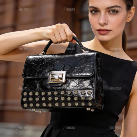 Model holding a black leather handbag adorned with stylish rivet studs, showcasing sophistication and elegance.