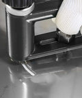 Adjustable sheet metal hole cutter in a black frame with two drill bits; gloved hand near the chuck.