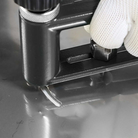 Adjustable sheet metal hole cutter in a black frame with two drill bits; gloved hand near the chuck.