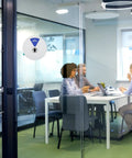 Six Status Six Inch Silver Office Door Sign with Working Remotely status on a glass door of a meeting room with people inside.