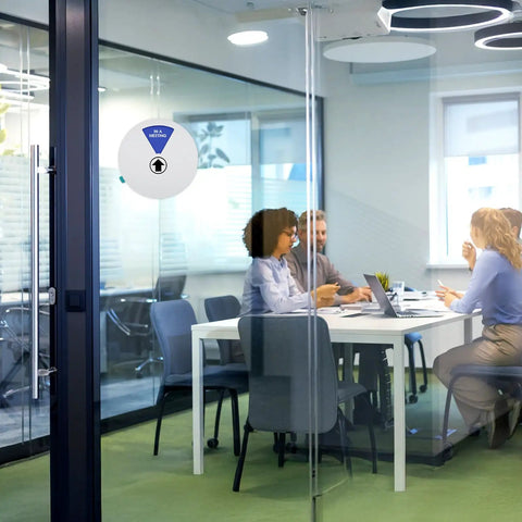 Six Status Six Inch Silver Office Door Sign with Working Remotely status on a glass door of a meeting room with people inside.