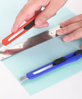 Hands using 24 Pack 9mm Wide Box Cutters Retractable Utility Knife Set For Heavy Duty Office Home Use Arts Crafts And DIY Projects Grab And Go Grips Workhorse Design Extended Use With Disposable Blades to cut paper.