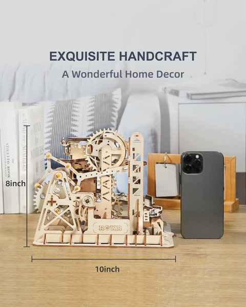 Fortress Tower Marble Run Puzzle Kit With Interlocking Gear Mechanics 3D Wooden Coaster Build displayed on a table next to a smartphone.