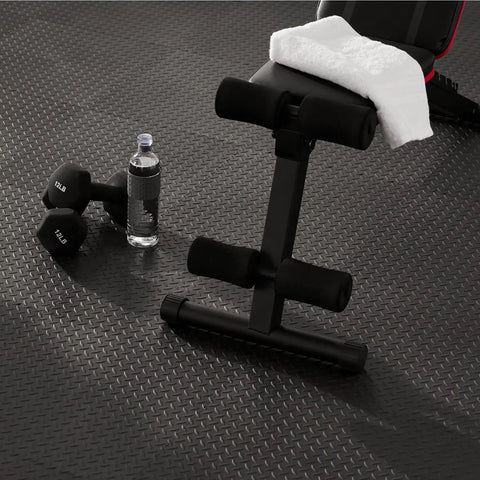 Interlocking Rubber Floor Tiles 18x18 Inch Diamond Plate Squares That Are Tough-As-Nails For Home Gym Garage Basement And Trade Show Floors, Durable Puncture-Resistant Mats, 24 Pack Black with exercise bench and weights on top.