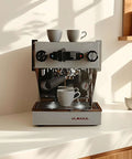 La Marzocco espresso machine brewing coffee, with two cups on top, in a bright kitchen setting.