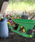 Person gardening with the Effortless Hand Crank Seed Spreader 1.5L for Garden and Lawn placed on soil, surrounded by flowers.