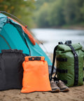 Three Six Pack Ultralight Dry Bags for Outdoors in black, orange, and green by a tent and river, Roll Top Waterproof Sacks Made Of Polyester With PU Coating, Keeps Gear Dry In Light Rain And Humidity