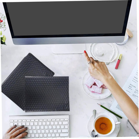 25 Pack Black Bubble Mailers Padded Envelopes Beefed Up Thickened Poly Bubble Packaging Bags on desk next to keyboard and tea