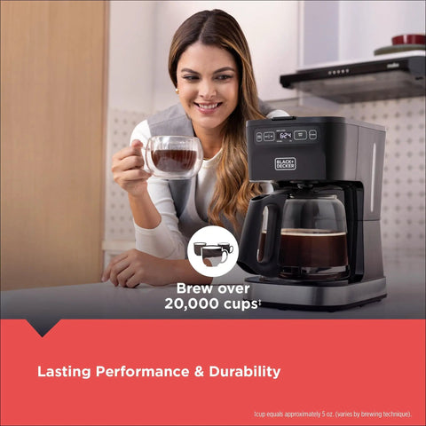 Woman enjoying coffee with CafeCraft 12 Cup Programmable Coffee Maker With Stainless Steel Drip Design on kitchen counter.