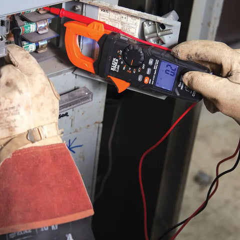 Electrician using a Digital Clamp Meter With Auto Ranging TRMS to measure voltage on a panel, showing AC/DC current reading.