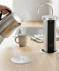 Pop Up Countertop Power Outlet With USB C And Four AC Sockets Slick Recessed Receptacle Pull Up Socket 10W Wireless Charger Easy Install For Kitchen Office Or Conference Room displayed on a kitchen counter next to a kettle pouring hot water.