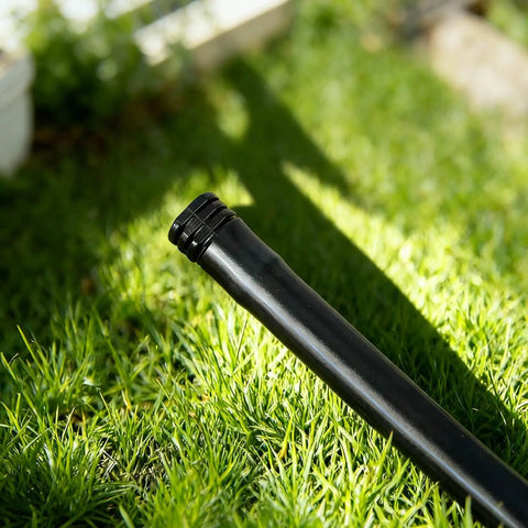 20 Pack 1/2 Inch Drip Irrigation Barbed End Plug Fittings And End Cap Connectors For 1/2 Inch Tubing 0.520 To 0.650 ID OD Garden Lawn Irrigation System No Fuss Setup installed on black tubing in a grassy garden.