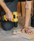 Side view of a yellow cordless drill with a blue twist drill bit drilling into a wooden block