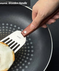Slotted fish spatula with wooden full-tang handle and stainless steel blade flipping a fried egg in a pan