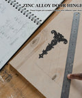 Vintage Style Black Zinc Alloy Tee Door Hinges on workshop table with ruler and notebook, ideal for cabinets and sheds.