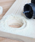 Black hole saw bit cutting a hole in a wooden board with sawdust around