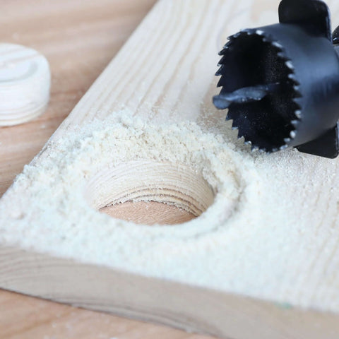 Black hole saw bit cutting a hole in a wooden board with sawdust around
