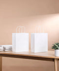 White Kraft Paper Gift Bags With Handles Pack Of 25 Medium 8 By 4.5 By 10 Inches on table with plant