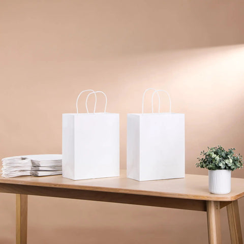 White Kraft Paper Gift Bags With Handles Pack Of 25 Medium 8 By 4.5 By 10 Inches on table with plant