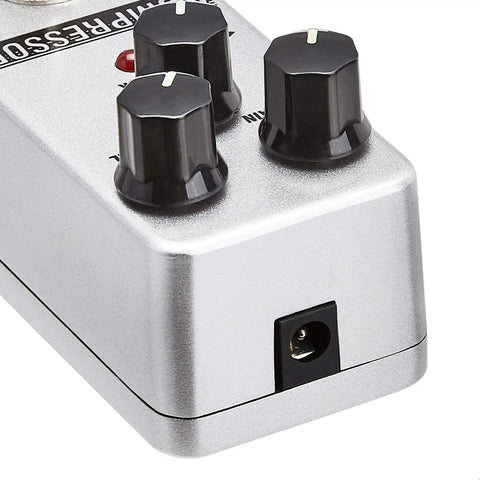 Close-up of a compact analog guitar compressor pedal with true bypass, sleek silver finish, and durable aluminum build featuring knobs and input jack.