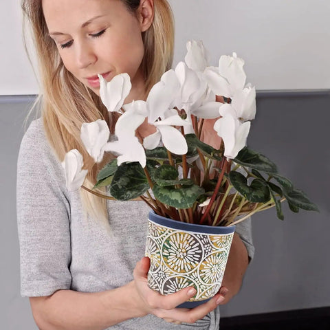 Woman holding a plant in a decorative ceramic pot indoors