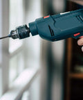 Side view of a blue cordless power drill with metal chuck and bit.