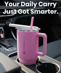 Pink HydroJug tumbler with handle in a car cup holder, featuring a straw and lid; "Your Daily Carry Just Got Smarter." message visible.