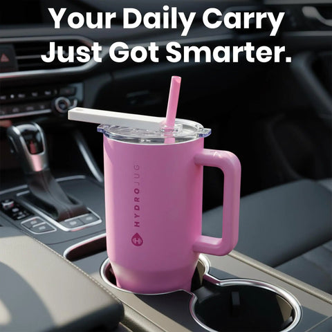 Pink HydroJug tumbler with handle in a car cup holder, featuring a straw and lid; "Your Daily Carry Just Got Smarter." message visible.