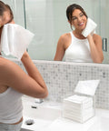 Woman using a facial wipe in front of a mirror with the No Fuss Clear Acrylic Storage Box For Towels And Towelettes Countertop Dispenser Bin.