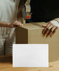 Rigid Self Seal Mailers 90 Pack White Cardboard Envelopes in front of a packed cardboard box being sealed with tape