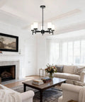 Matte Black Five Light Chandelier With Dual Glass Shades hanging in a modern farmhouse living room, slim arms, adjustable height.