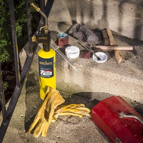 Trigger Start Butane Torch for Soldering and Welding with MAP PRO gas, tools, and gloves on a concrete step in a DIY setup