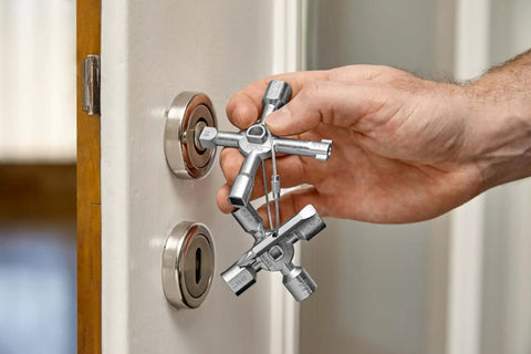 Hand holding TwinKey Multifunctional Spanner Kit with Magnetic Eight Arm Two By Four Way Spider Keys, near a control cabinet lock.