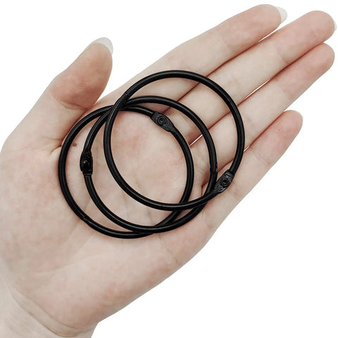 Hand holding black rustproof metal shower curtain hooks 24 pack that glide smoothly round rings for curtains on a bathroom shower rod.